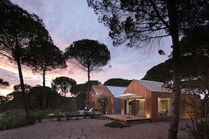 A modern wooden cabin with a large glass door, surrounded by trees and a sandy area. - Sublime Comporta  (Grandola)