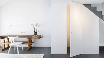 A modern interior with a wooden desk, white chairs, and a potted plant.
