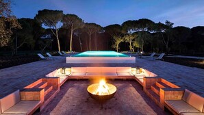 Un área junto a la piscina con una chimenea, sillones de descanso y una pileta.