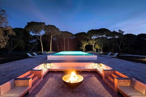 A poolside area with a fire pit, lounge chairs, and a swimming pool.