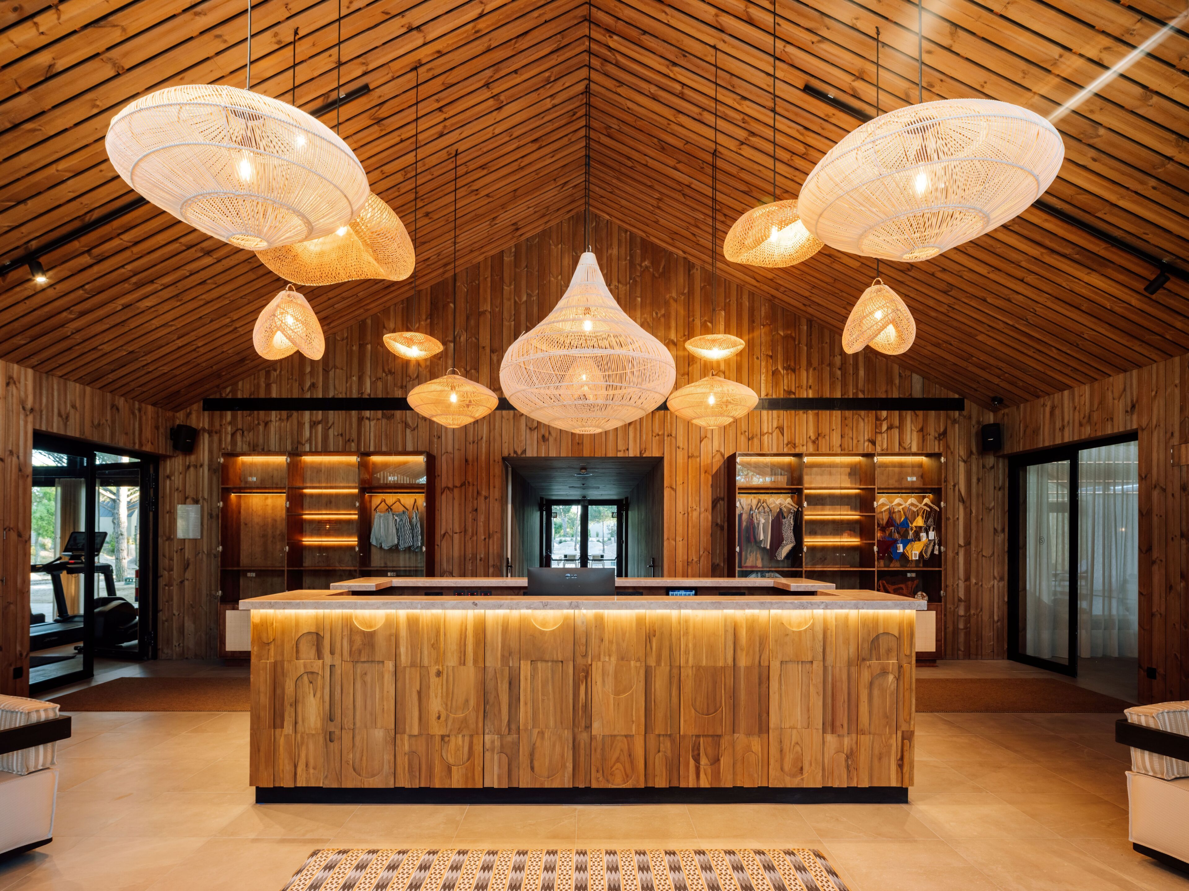 A wooden interior with a central reception desk, pendant lighting, and clothing displays.