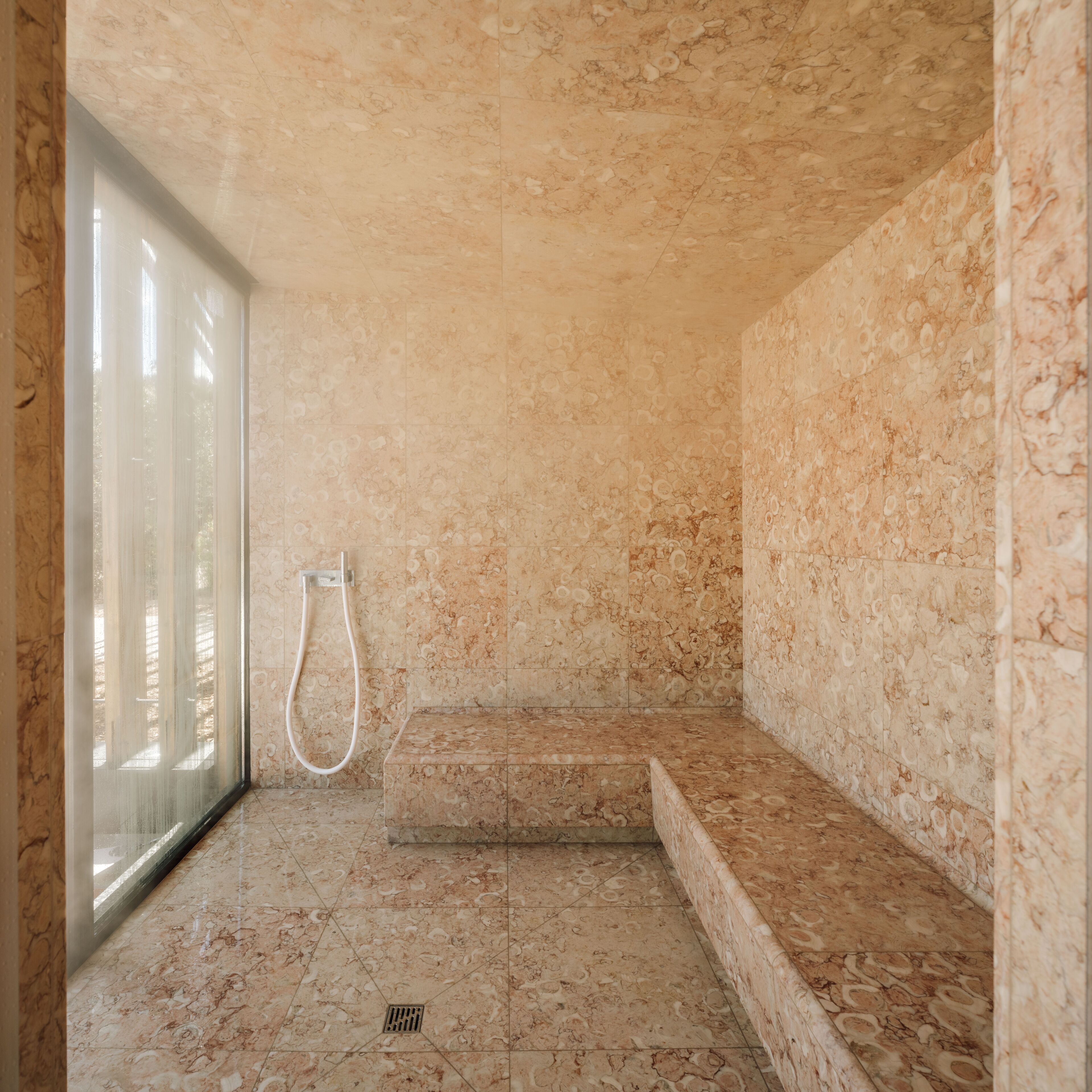 A bathroom with a shower, a window, and a marble floor.