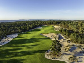 A golf course with sand bunkers, a water hazard, and a forested area.