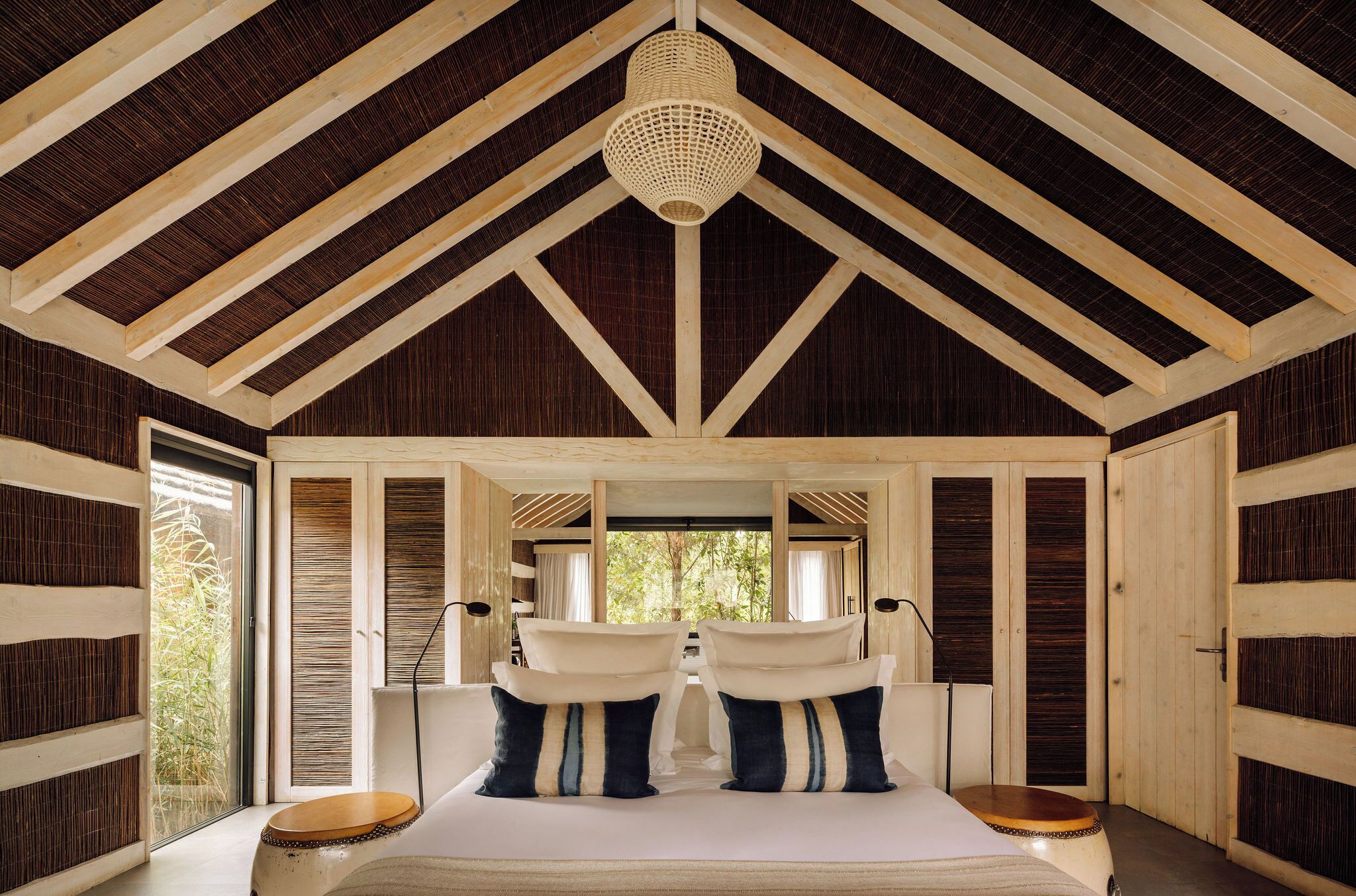 A bedroom with a high ceiling, wooden beams, a bed with pillows, and a window.