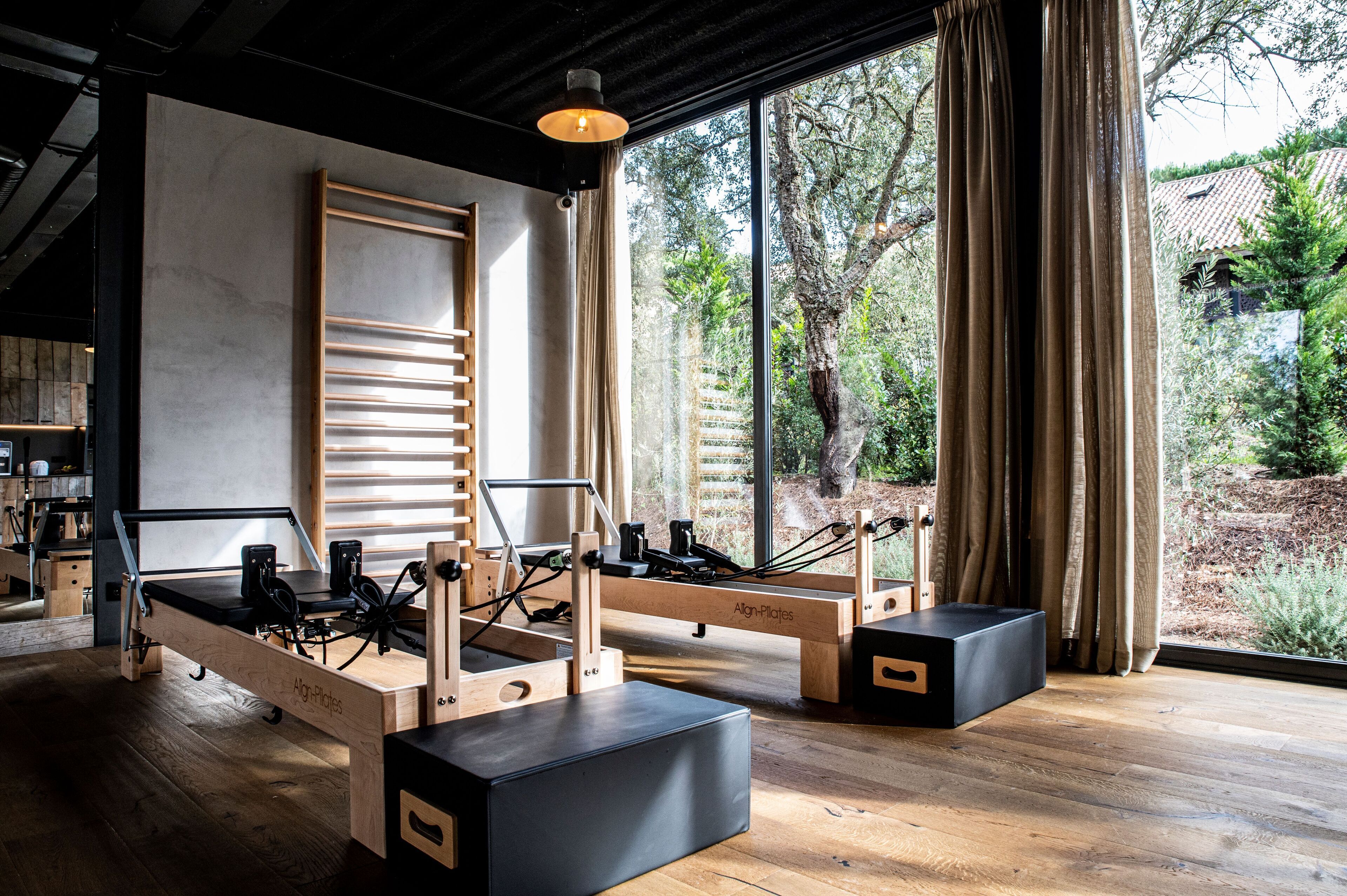A Pilates studio with wooden equipment, large windows, and a view of trees.