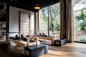 A Pilates studio with wooden equipment, large windows, and a view of trees.