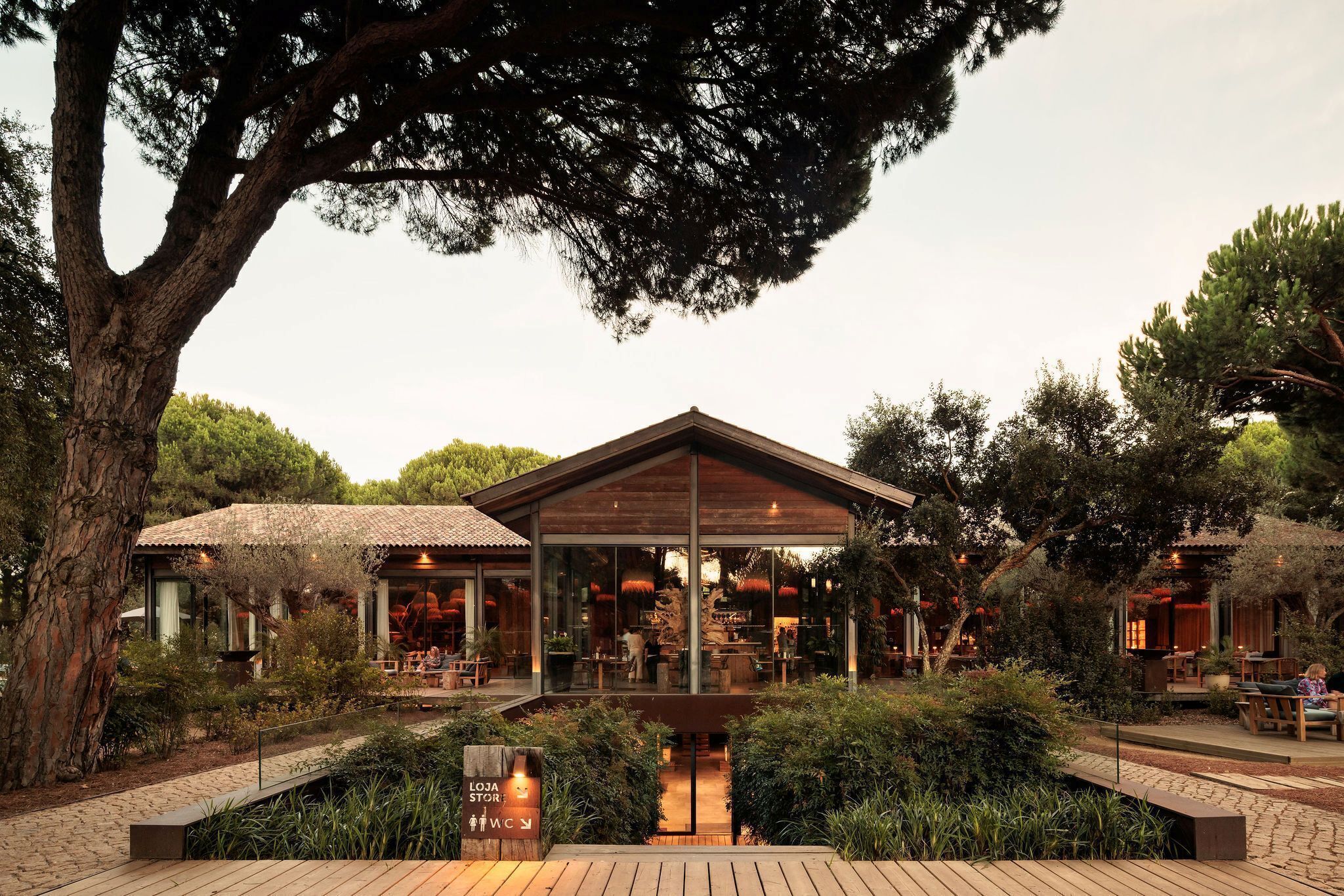 A modern building with a glass facade, surrounded by lush greenery and trees.