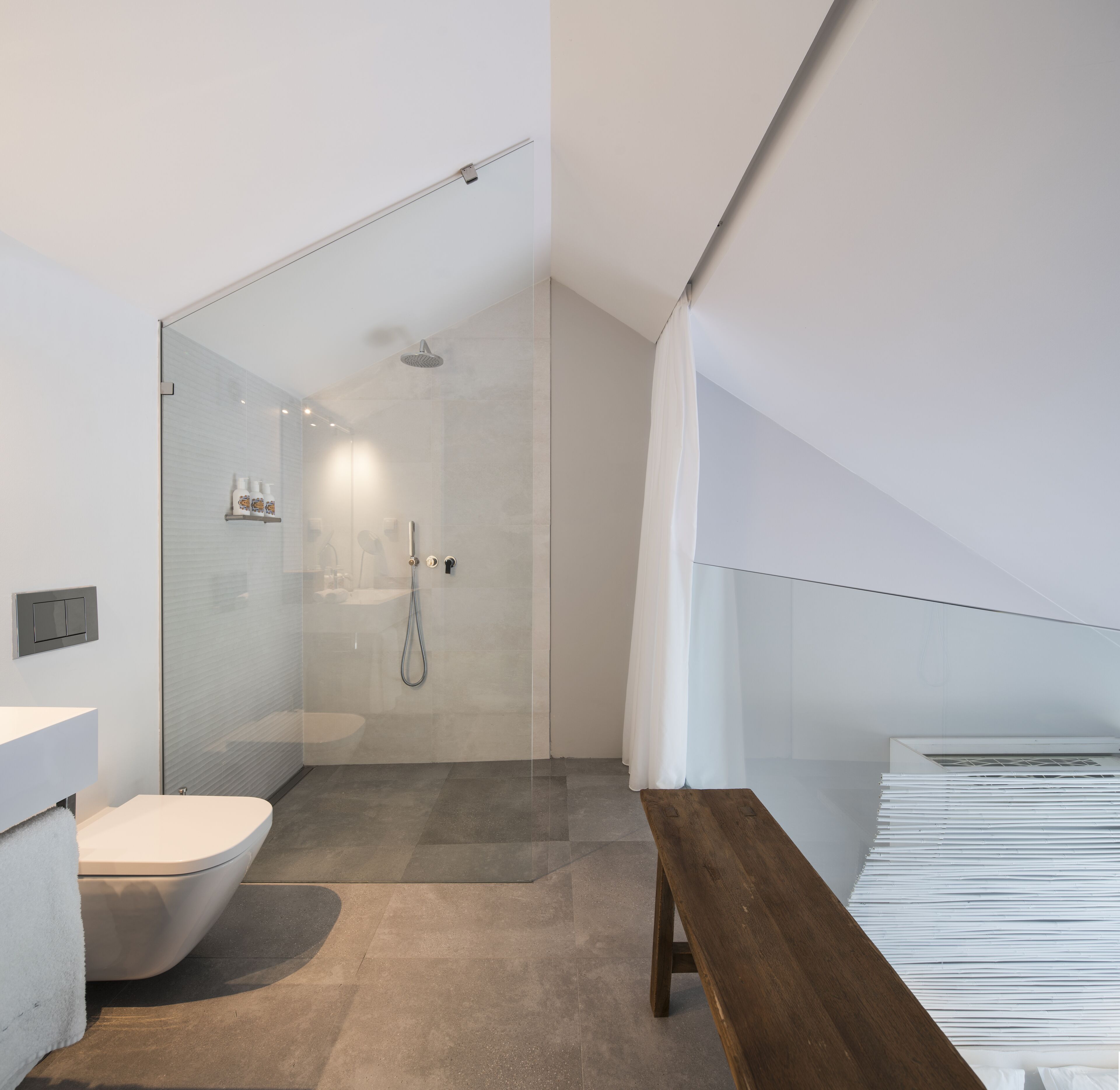 A modern bathroom with a glass shower enclosure, a toilet, and a wooden bench.