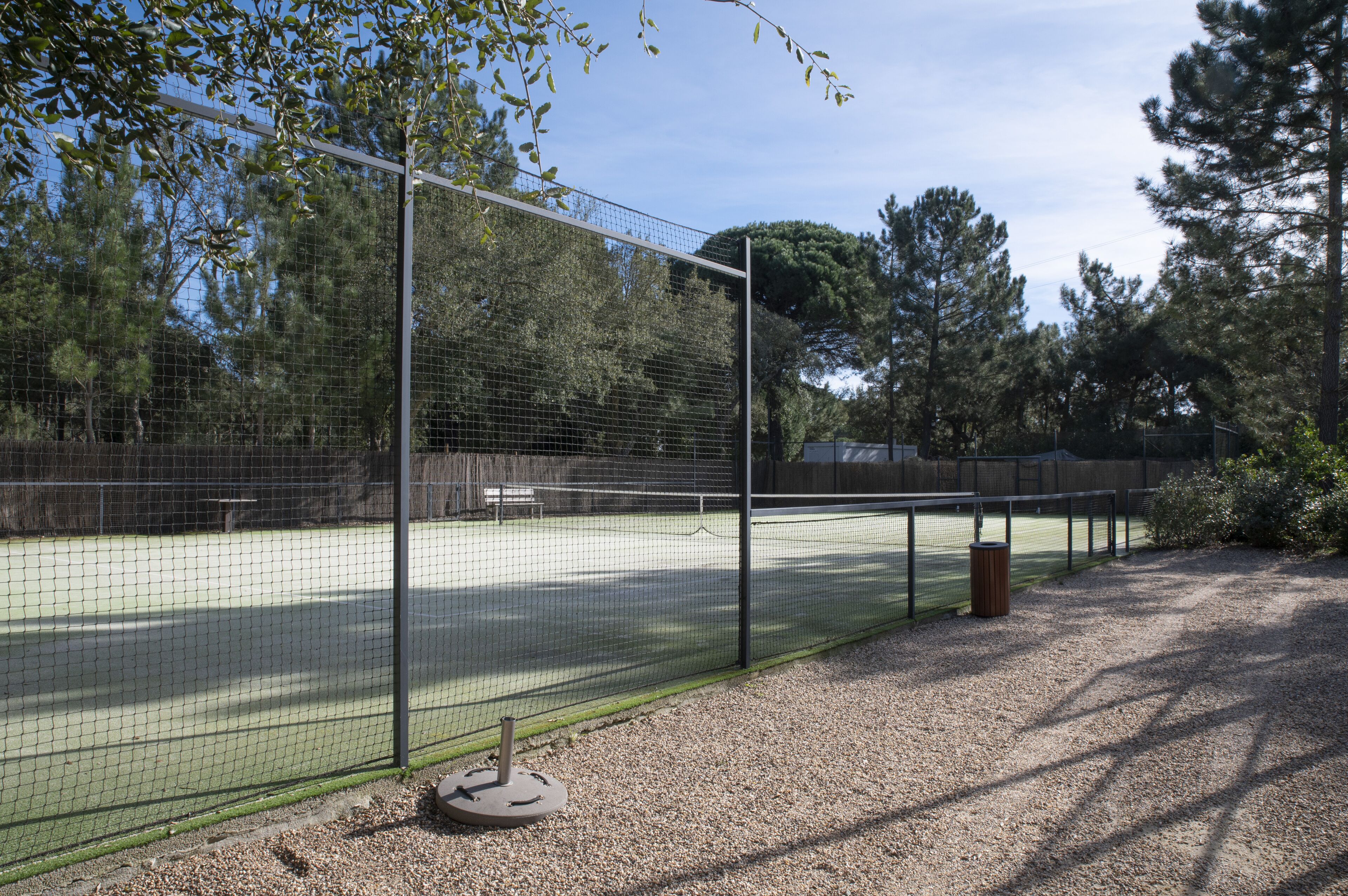 A tennis court enclosed by a wire fence with trees in the background.