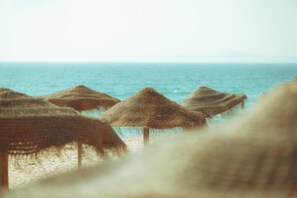 Una playa con sombrillas de paja y el mar al fondo.
