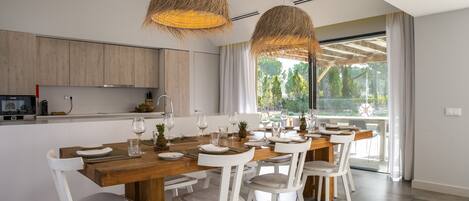 Una cocina moderna con armarios de madera, una mesa de comedor para seis personas y ventanas amplias con vistas a la vegetación.