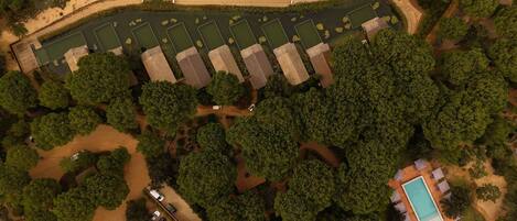 An aerial view of a resort with multiple buildings, a swimming pool, and a parking area surrounded by dense trees.