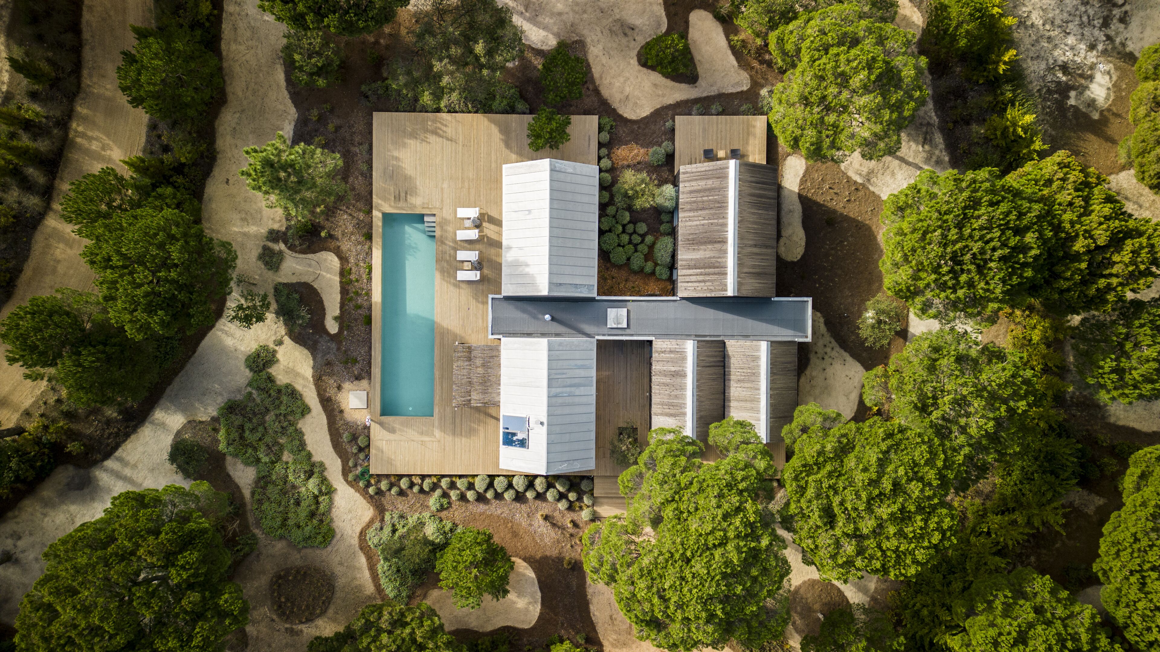Vista aérea de una casa moderna con piscina, mobiliario de exterior y jardín.