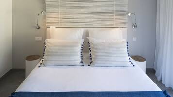 Una cama bien tendida con ropa de cama blanca y detalles azules, dos lámparas de noche y una ventana con persianas.
