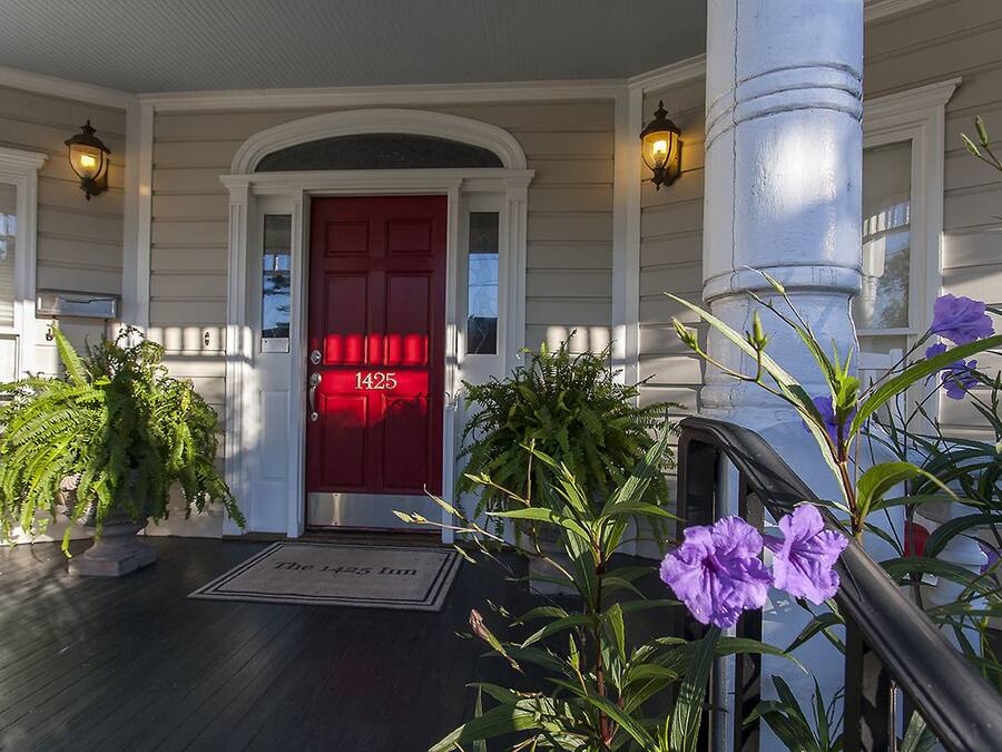A red door with the number 1425 on it, a white porch with a black railing, and two potted plants.