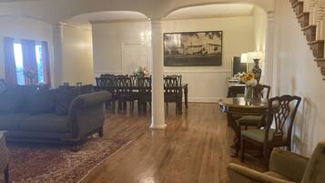 Un salón amplio con piso de madera, una zona de comedor con mesa y sillas, y una escalera con barandilla decorativa.
