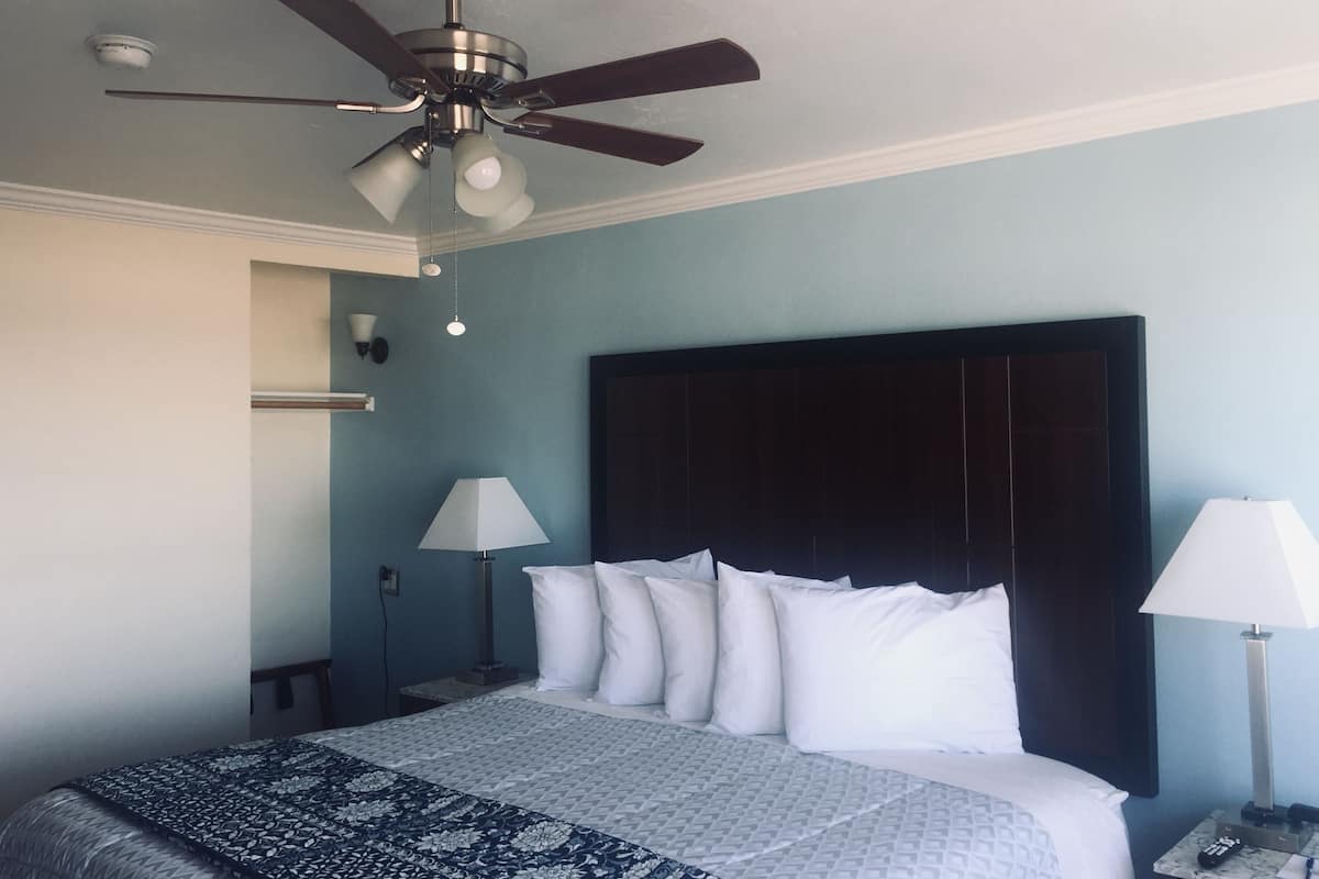 Een hotelkamer met een bed, een plafondventilator, een nachtkastje en een lamp.