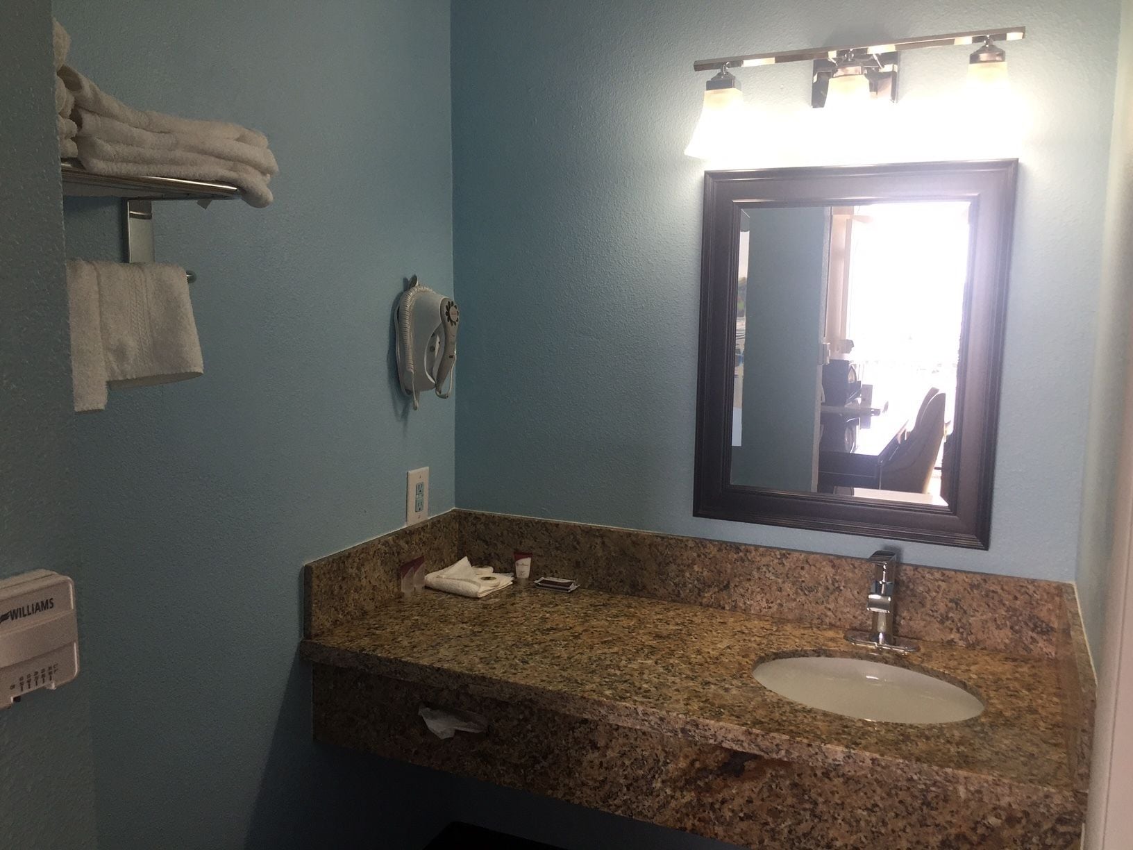Un baño con lavamanos de encimera de granito, espejo y toallero.