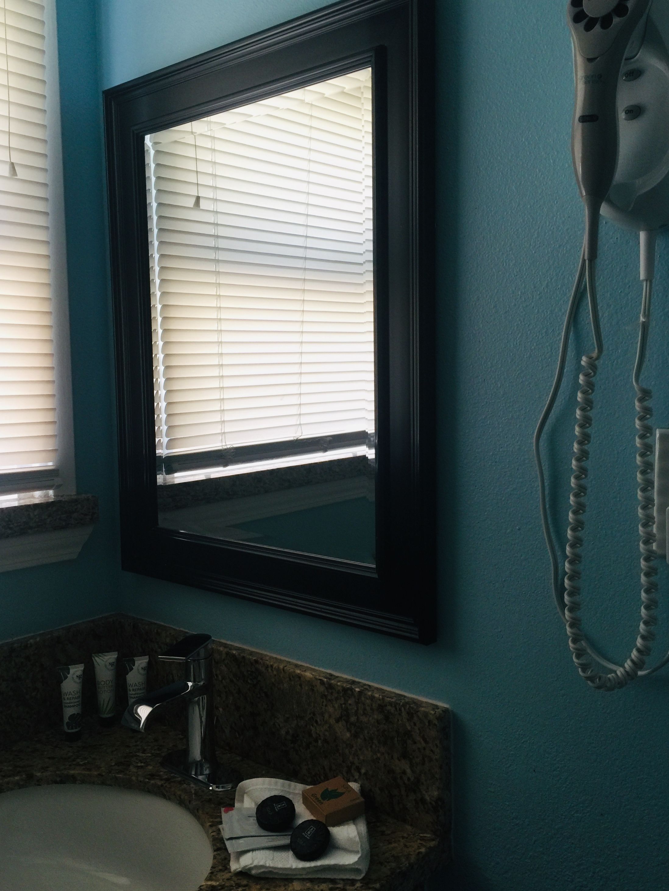 Une salle de bain équipée d’un lavabo, d’un sèche-cheveux et d’une fenêtre avec des stores.