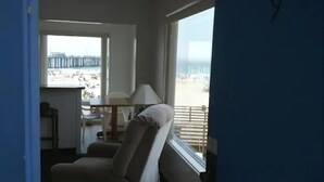 Une chambre avec vue sur la plage, un canapé, une table avec une lampe et une fenêtre avec des stores.