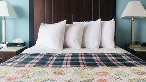 Une chambre d’hôtel avec un grand lit, une tête de lit en bois sombre, des oreillers blancs, une couvre-lit à carreaux et des lampes de chevet.