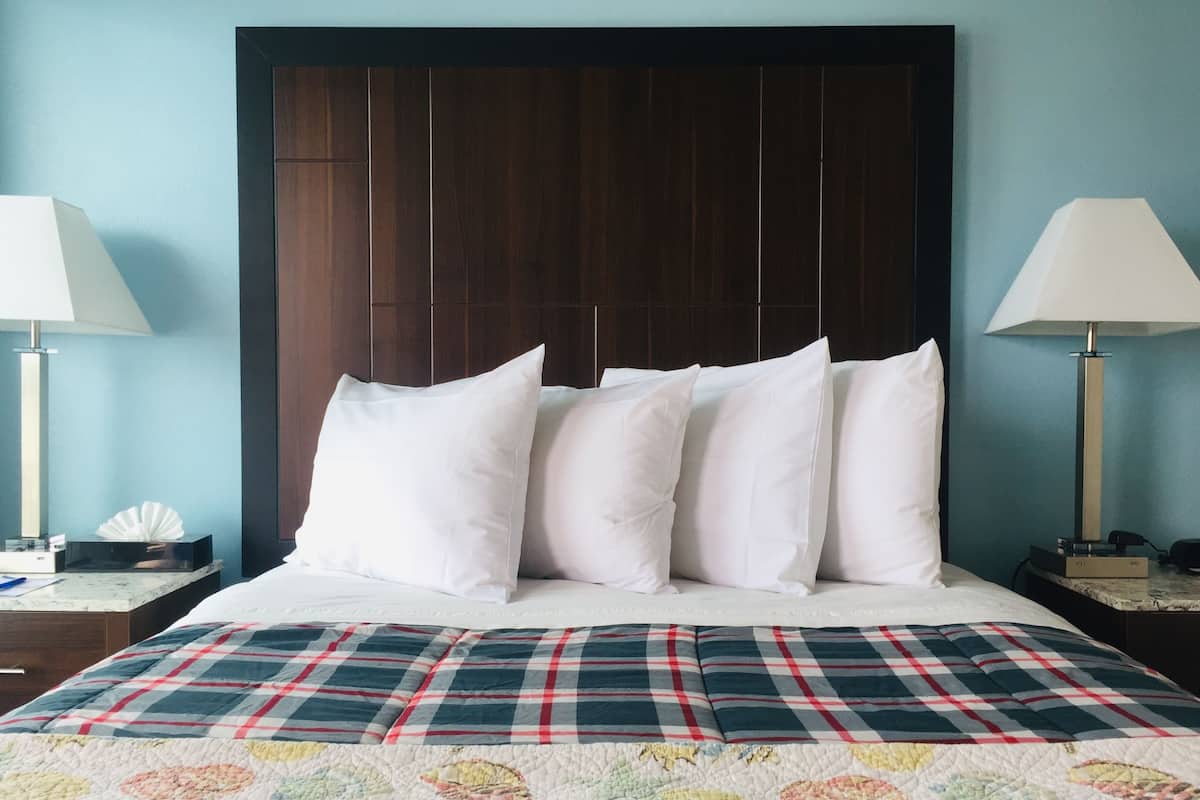 Een hotelkamer met een groot bed, een donker houten hoofdbord, witte kussens, een geruit sprei en nachtlampjes.