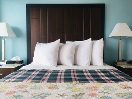 A hotel room with a large bed, a dark wooden headboard, white pillows, a plaid bedspread, and bedside lamps.