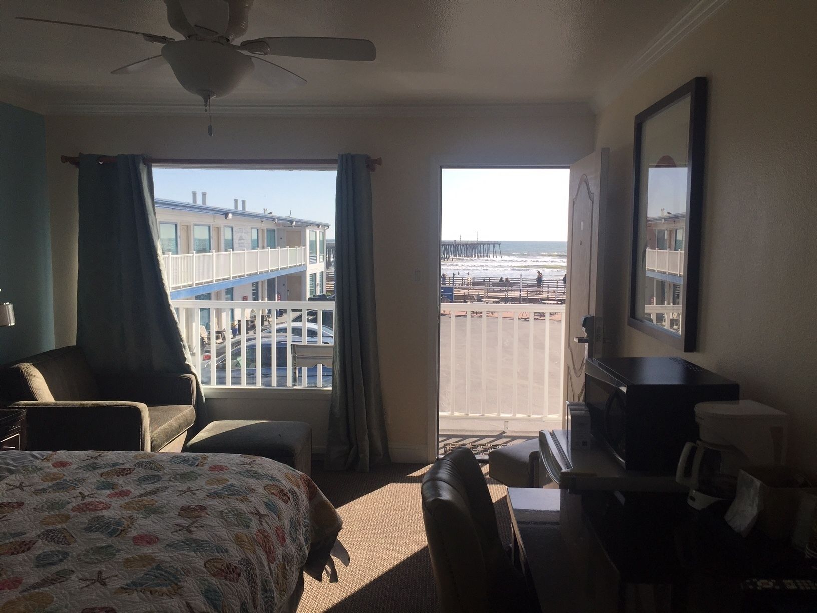 Habitación de hotel con cama, escritorio, silla y vista a la playa y al muelle.