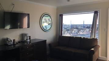 A hotel room with a sofa, a TV, a coffee maker, and a window with a view of the outside.