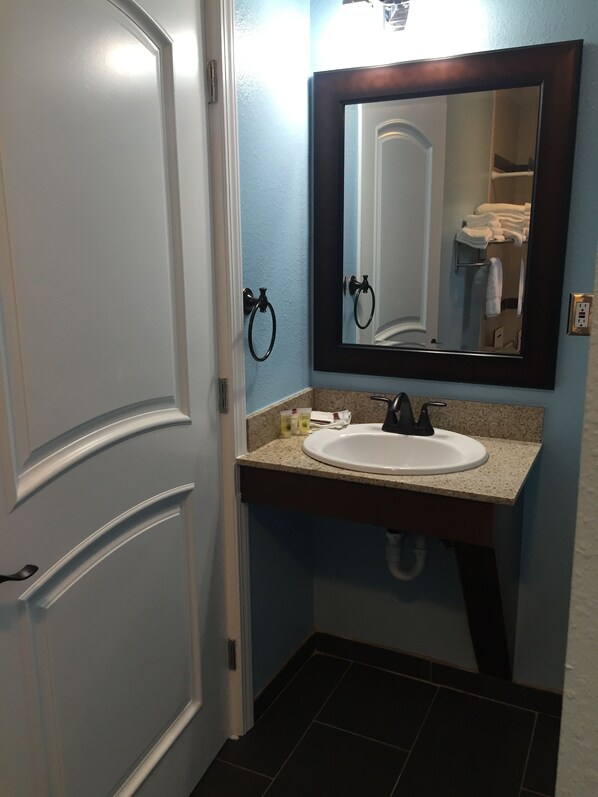 A bathroom with a white sink, dark countertop, and a large mirror above it.