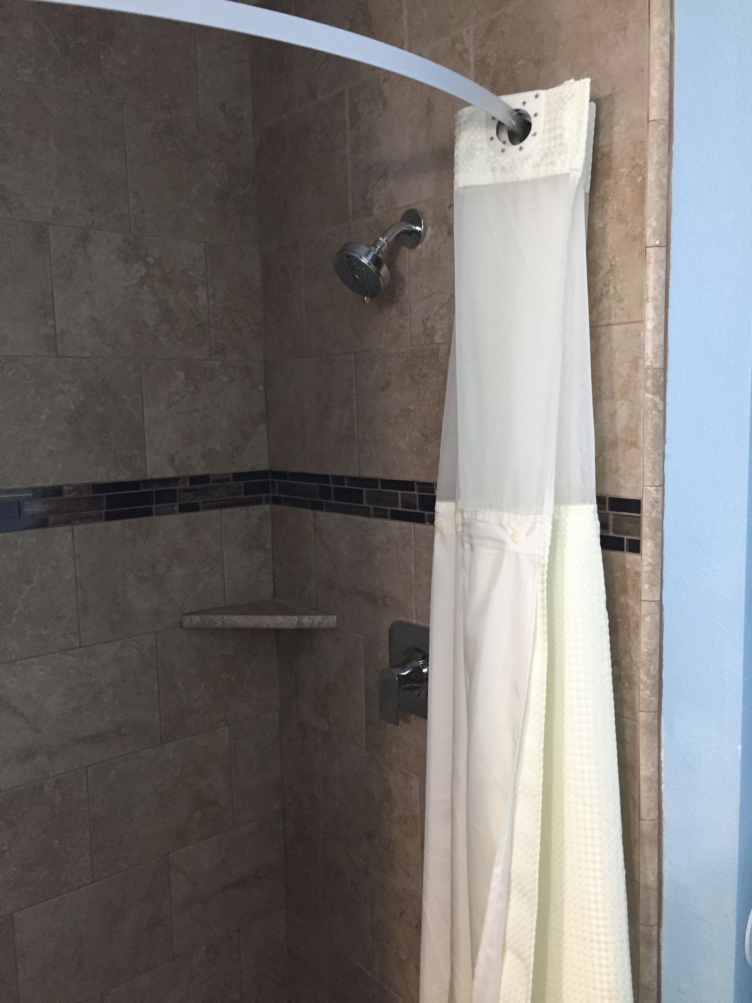 A shower area with a tiled wall, a showerhead, and a white shower curtain.