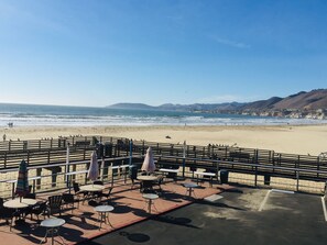 A beachside patio with tables and chairs, overlooking the ocean and hills.
