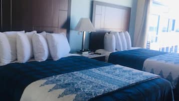 A hotel room with two beds, a nightstand with a lamp, and a view of the outside.