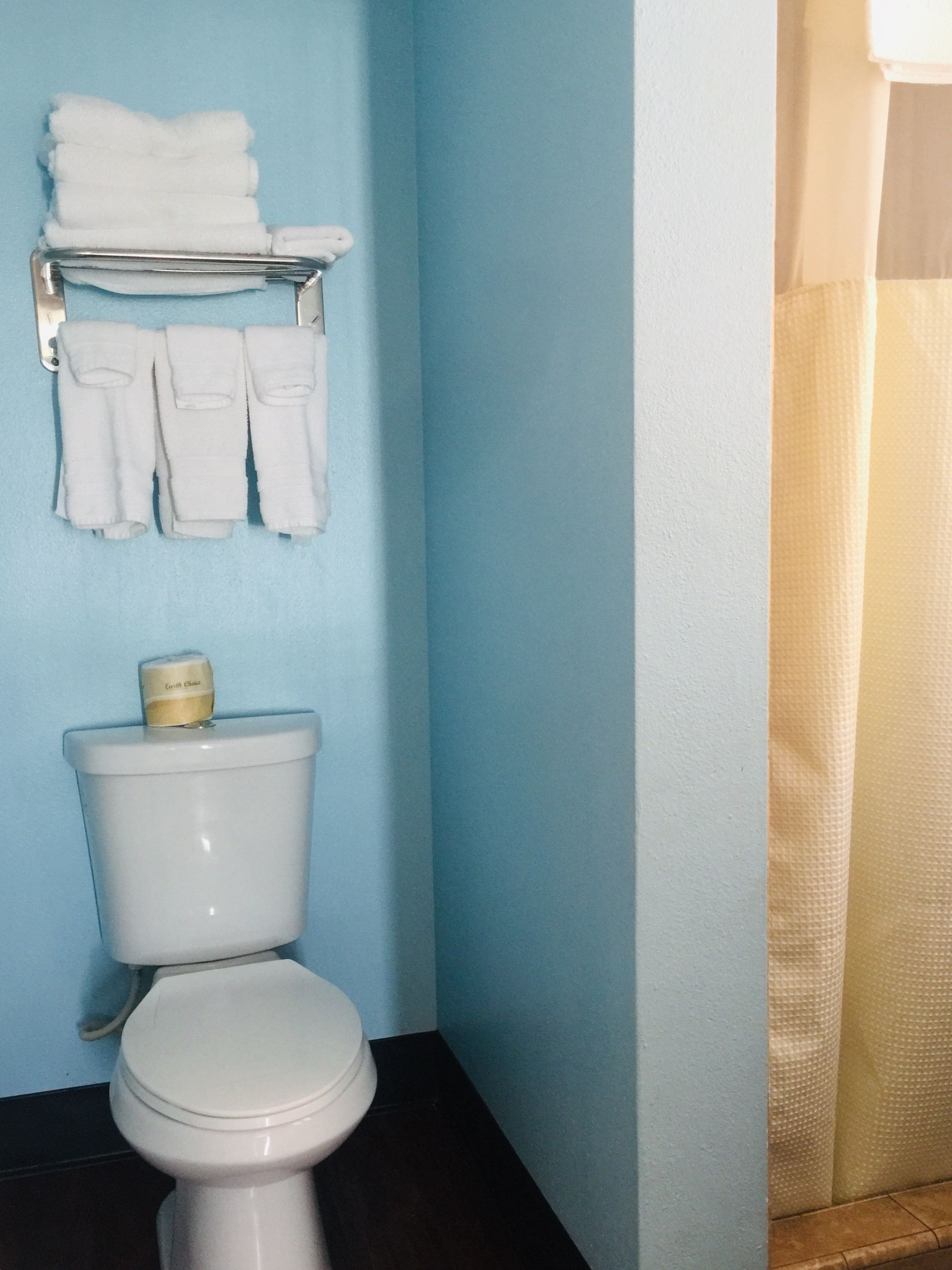 Une salle de bain équipée de toilettes, d’un porte-serviettes avec des serviettes pliées et d’un support à papier toilette.