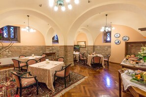 Enjoy meals in this elegant dining area with arched ceilings and stone walls, surrounded by classic chairs and decorative plates.