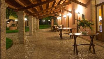 A covered outdoor patio area with stone flooring, wooden tables, and chairs, and a potted plant on one table.