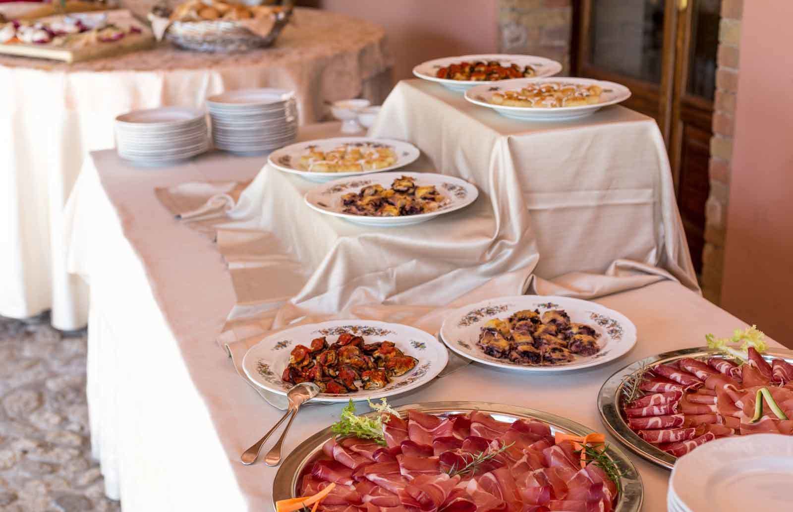 Una mesa de buffet con diversos platos, entre ellos carnes y pasteles, cubierta con manteles blancos.