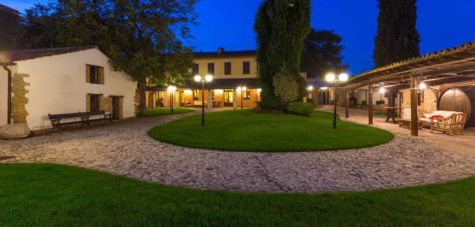 Un patio con un camino de piedra, una zona verde y un edificio con varias ventanas y un área de estar cubierta.