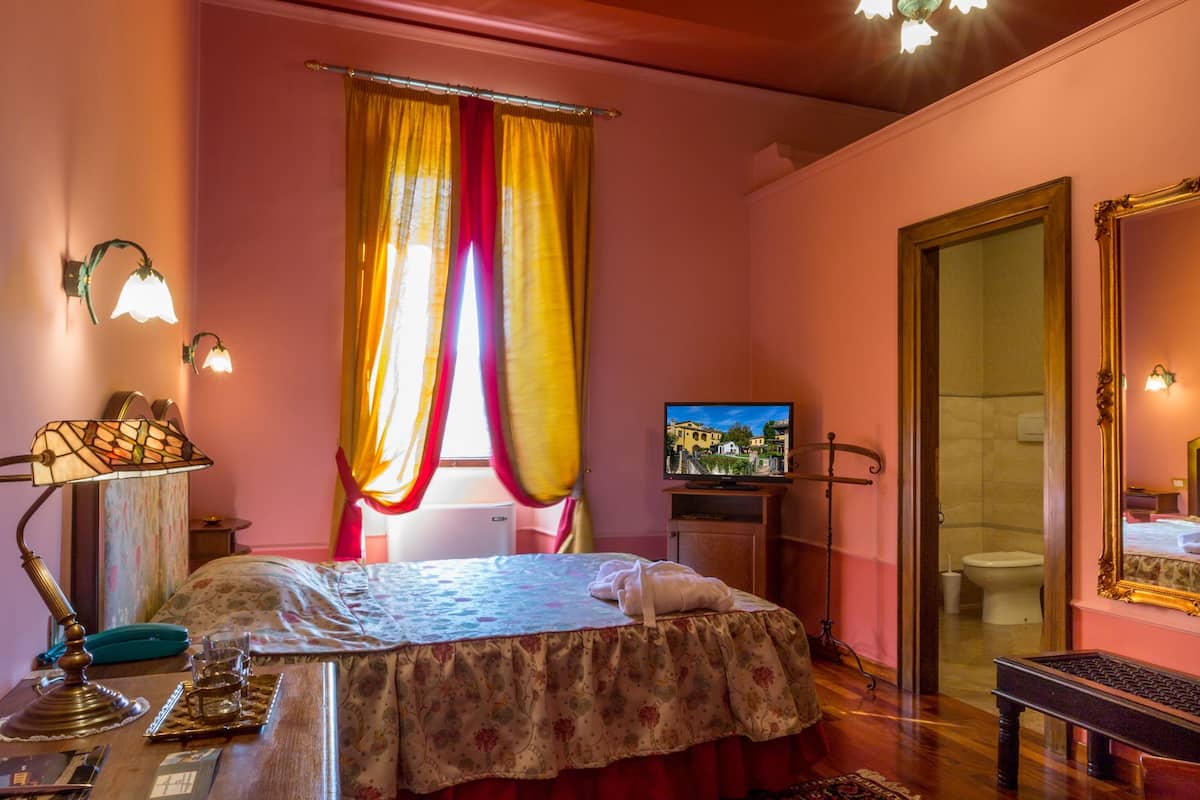 A bedroom with a bed, a desk, a television, and a bathroom visible through an open door.