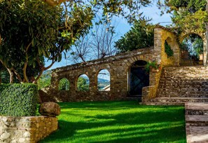 A stone bridge with three arches, a grassy area, and a stone wall with a large rock.