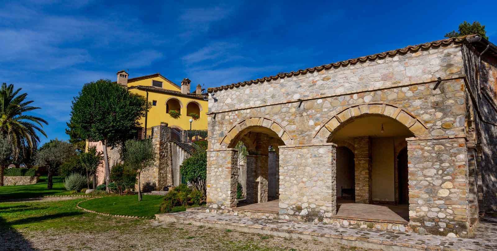 Un bâtiment en pierre, doté d’arcades, et un bâtiment jaune en arrière-plan.