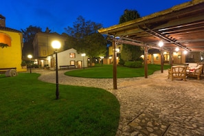 A courtyard with a stone pathway, a covered seating area, and a building with a yellow facade. - Corte dei Tini (Teramo)