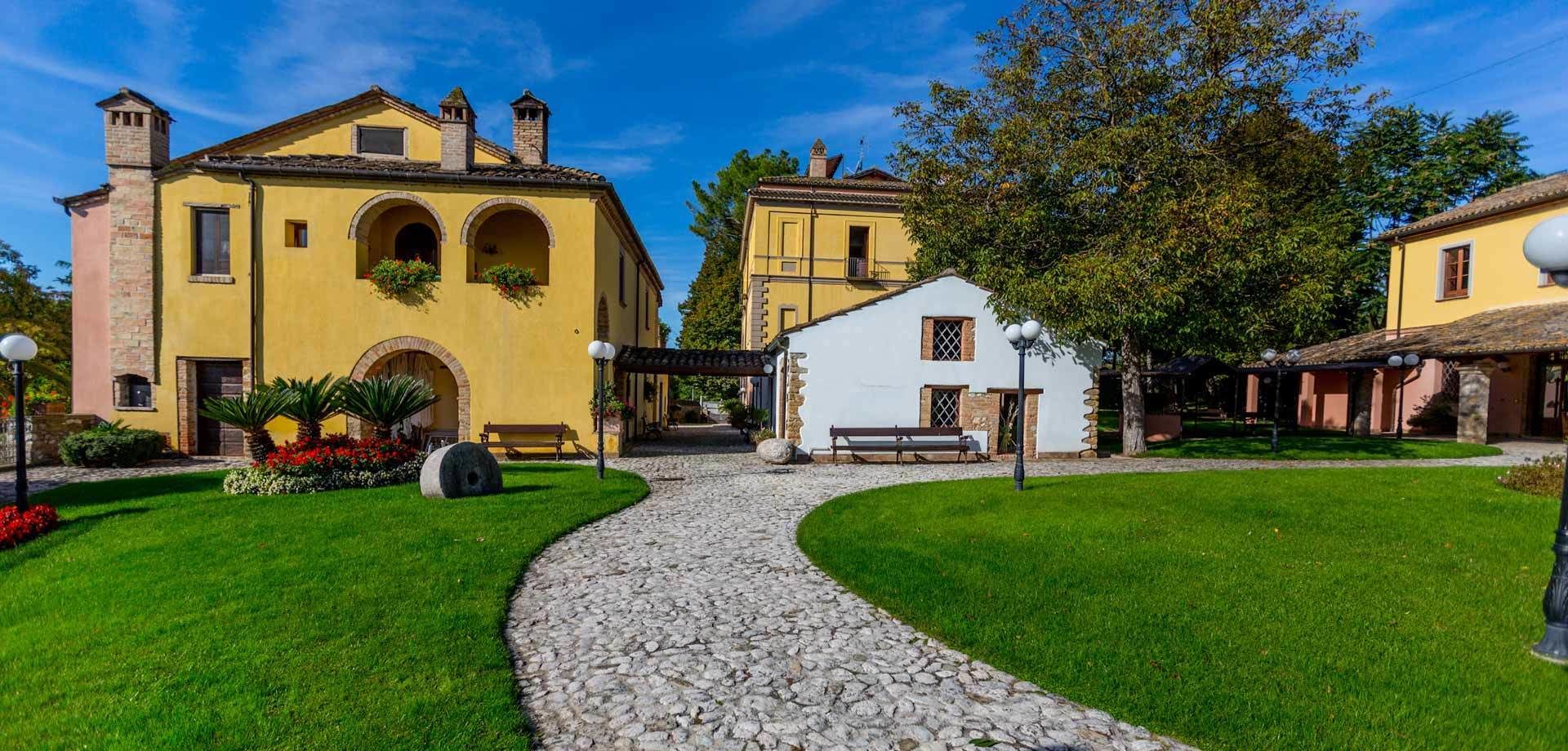 A courtyard with a cobblestone path, a yellow building with arches, and a white building with a balcony.
