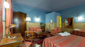 Una camera d'albergo con un letto, due poltrone, una scrivania in legno, una lampada, una televisione e un tappeto decorato.