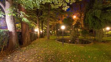 A nighttime park scene with trees, a circular pond, and street lamps.