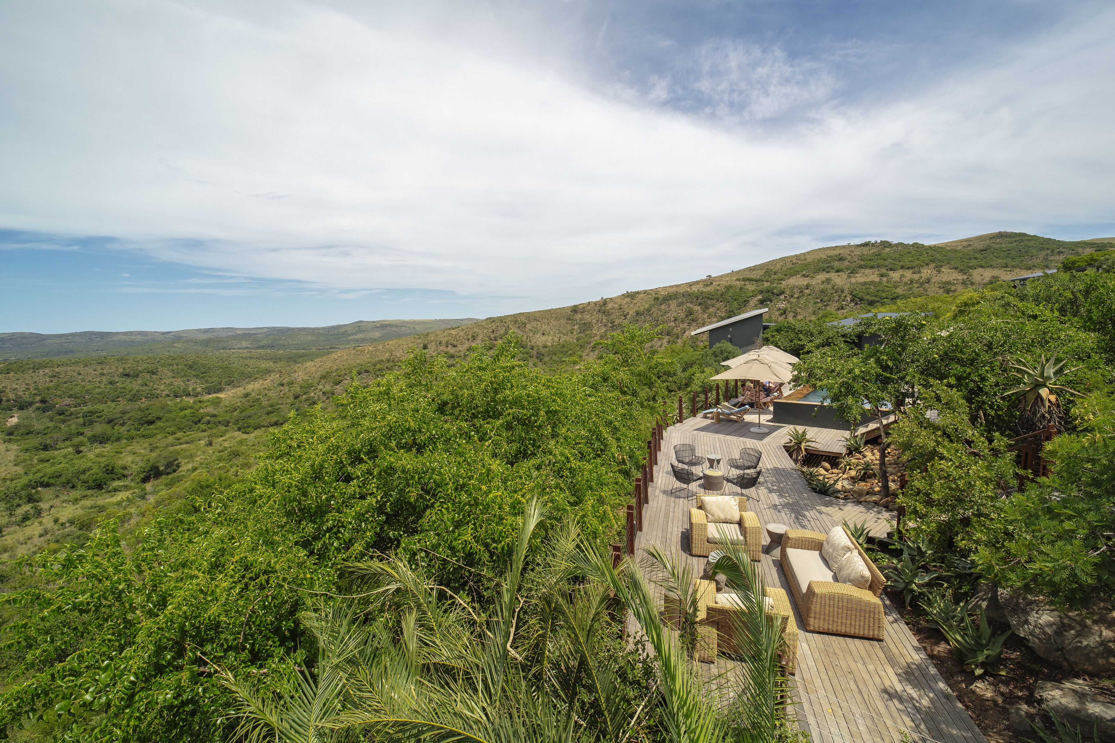 A wooden deck with outdoor seating, surrounded by lush greenery and hills in the background.