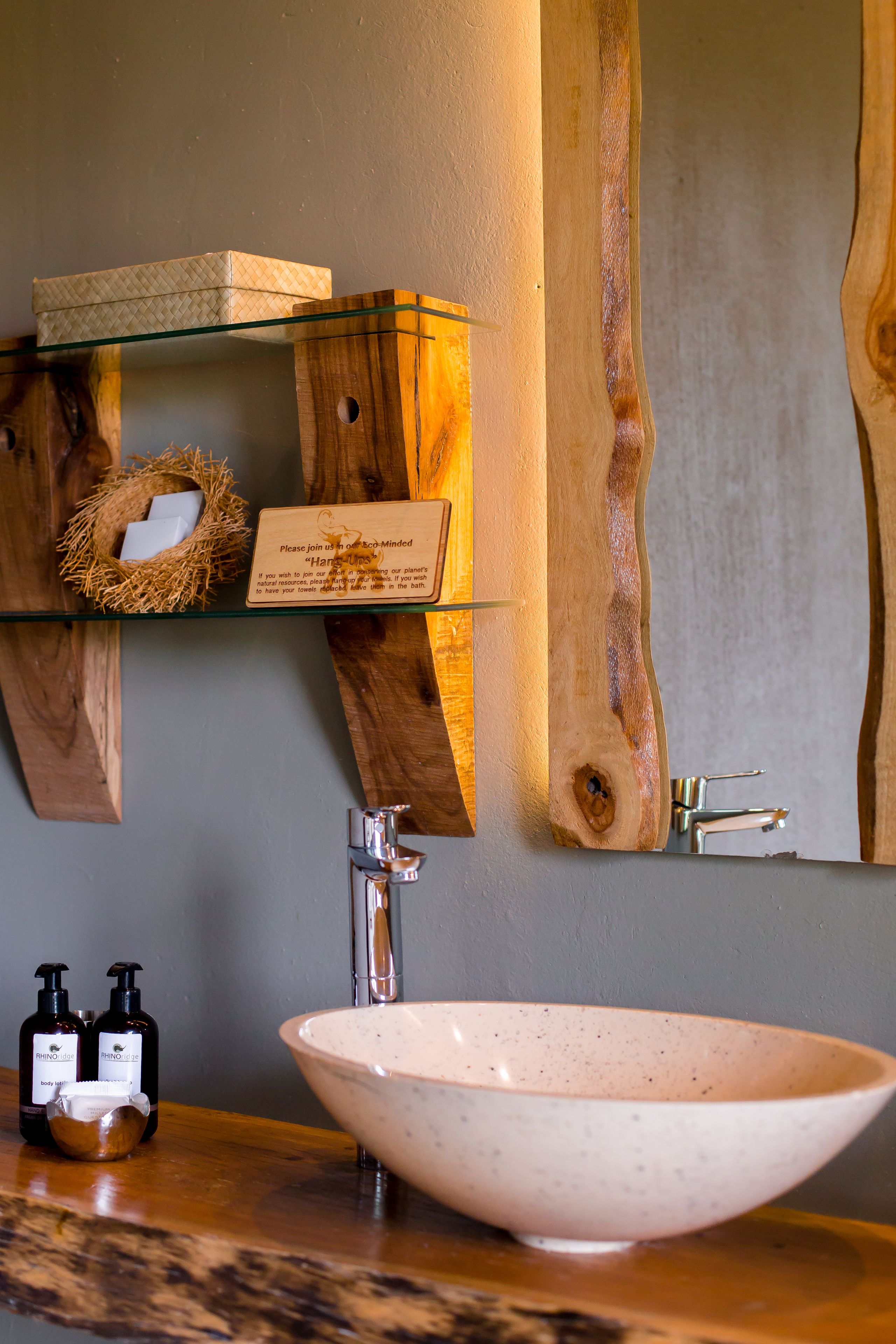 Une salle de bain avec un meuble-lavabo en bois, une étagère en verre où sont rangés les articles de toilette et un grand miroir.
