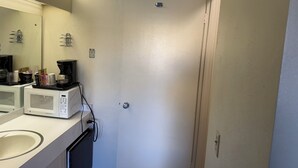 A compact bathroom with a white sink, a mirror, a coffee maker, and a microwave. - Down Towner Inn (Grangeville)