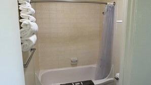 A bathroom with a bathtub, a shower curtain, and a towel rack with towels. - Down Towner Inn (Grangeville)