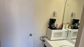 A small bathroom with a white sink, a mirror, a coffee maker, and a microwave. - Down Towner Inn (Grangeville)